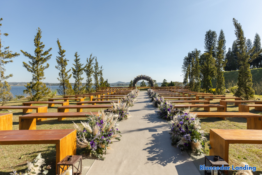Outdoor lakeside wedding ceremony setup with wooden benches, floral aisle décor, and rustic arch at Blue Cedar Landing