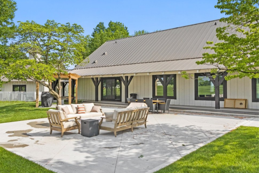 Outdoor patio at a wedding venue with guest lodging, lounge seating, dining area, green lawn, and mature trees
